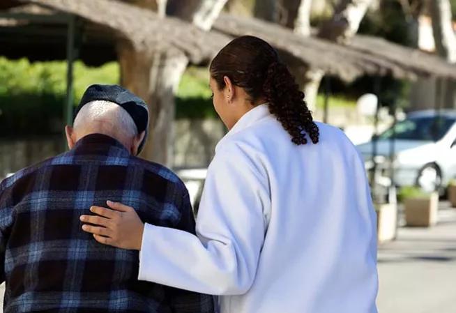 Visuel d'une personne âgée de dos accompagnée par une soignante