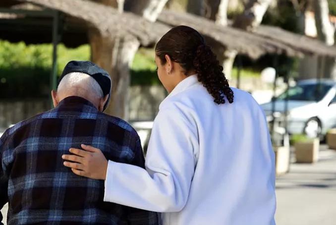 Visuel d'une personne âgée de dos accompagnée par une soignante